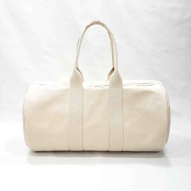 May include: A cream-colored canvas duffel bag with two long straps and a zipper closure.
