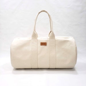 May include: A cream-colored canvas duffel bag with brown leather straps and a brown leather label that says "BLAKE".