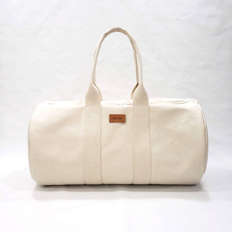 May include: A cream-colored canvas duffel bag with brown leather straps and a brown leather label that says "BLAKE".