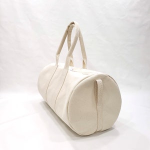 May include: A plain white canvas duffel bag with two top handles and a side strap.