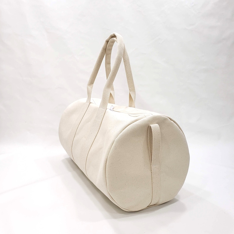 May include: A plain white canvas duffel bag with two top handles and a side strap.
