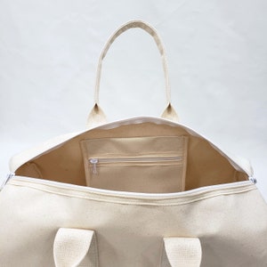 May include: A white canvas duffel bag with a zippered pocket on the inside. The bag has two handles and a zipper closure.
