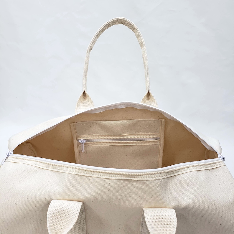 May include: A white canvas duffel bag with a zippered pocket on the inside. The bag has two handles and a zipper closure.