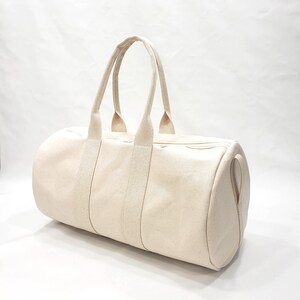 May include: A cream-colored canvas duffel bag with two top handles and a zipper closure.