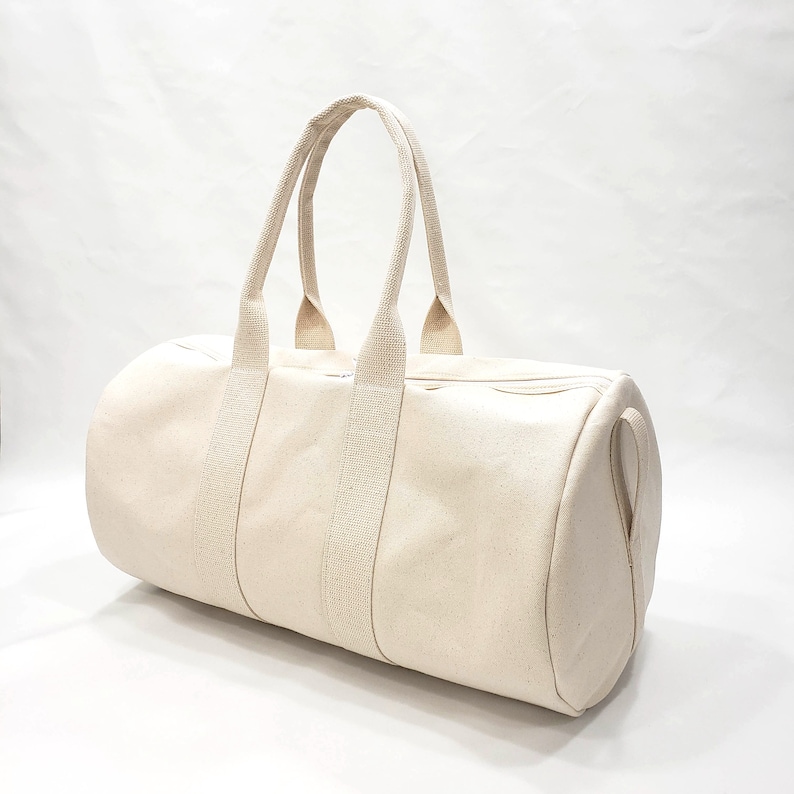 May include: A cream-colored canvas duffel bag with two top handles and a zipper closure.