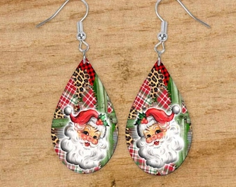 May include: Teardrop-shaped earrings with a Christmas theme. The earrings feature a Santa Claus design with a red hat and white beard, set against a plaid and leopard print background. The text "Earring Design for Sublimation" is at the top.