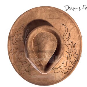 May include: A brown fedora-style hat with a wide brim. The hat features a black outline of a dragon on the left side and flames on the right. The text "Dragon & Fire" is written in black script on the upper right side.