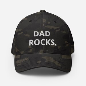 May include: A black and green camouflage baseball cap with the white text "DAD ROCKS."