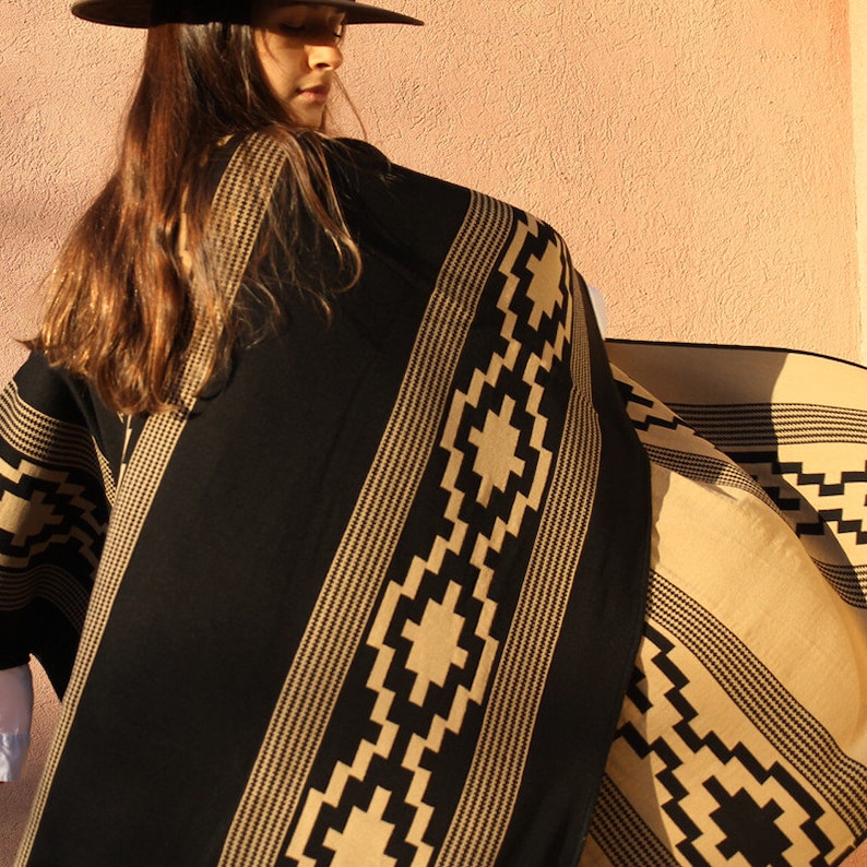 May include: A black and tan poncho with a geometric pattern. The poncho is made of a soft, woven fabric and has a fringed edge.