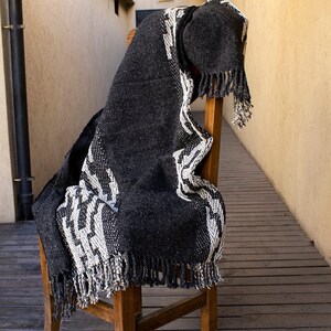 May include: Black and white woven throw blanket with fringe. The blanket is draped over a wooden chair.