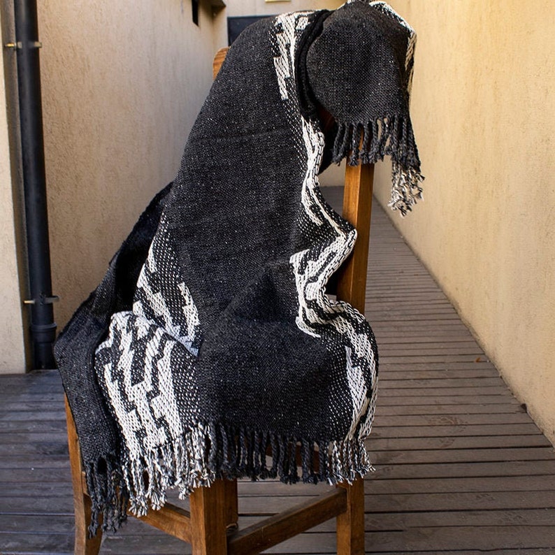 May include: Black and white woven throw blanket with fringe. The blanket is draped over a wooden chair.
