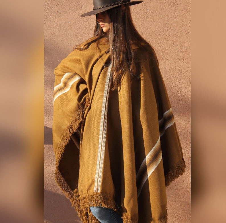 May include: A brown poncho with white and brown stripes and fringe trim. The poncho is worn by a person wearing a brown hat.