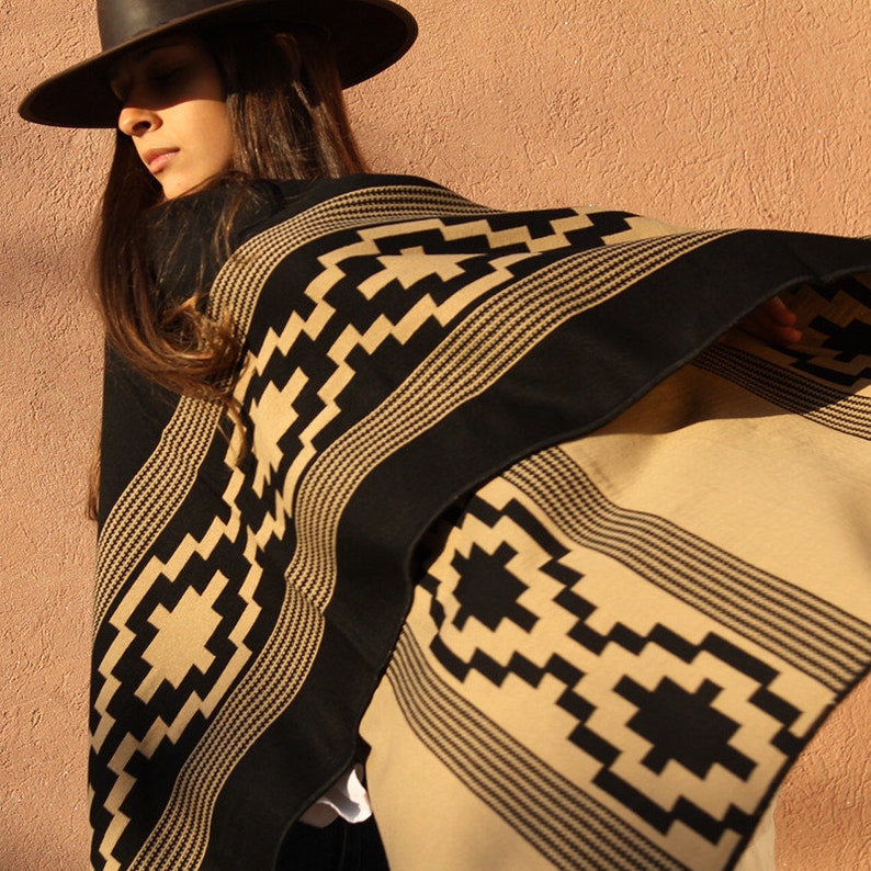 May include: A black and tan poncho with a geometric pattern. The poncho is worn by a person wearing a black hat.