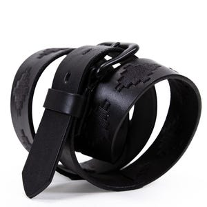 May include: A black leather belt with a matte black buckle. The belt features a geometric pattern embossed along its length. The belt is rolled up, showcasing the design and texture of the leather.