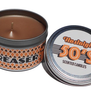 May include: A round tin candle with a black and orange label that says "Greaser" and a brown wax candle inside. The lid of the tin is silver and has a white label that says "Nostalgia 50's Scented Candles".