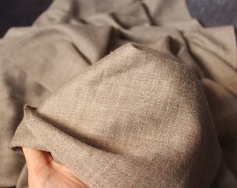 May include: Close-up of beige linen fabric, showing its textured surface. The fabric is draped and folded, revealing the natural weave and colour variations. The material appears soft and lightweight, suitable for clothing or home decor.