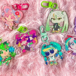 May include: A set of seven colourful anime character keychains with glitter accents. Each keychain features a different character with a unique design and pose. The keychains are made of clear acrylic and have metal rings for attaching to keys or bags.