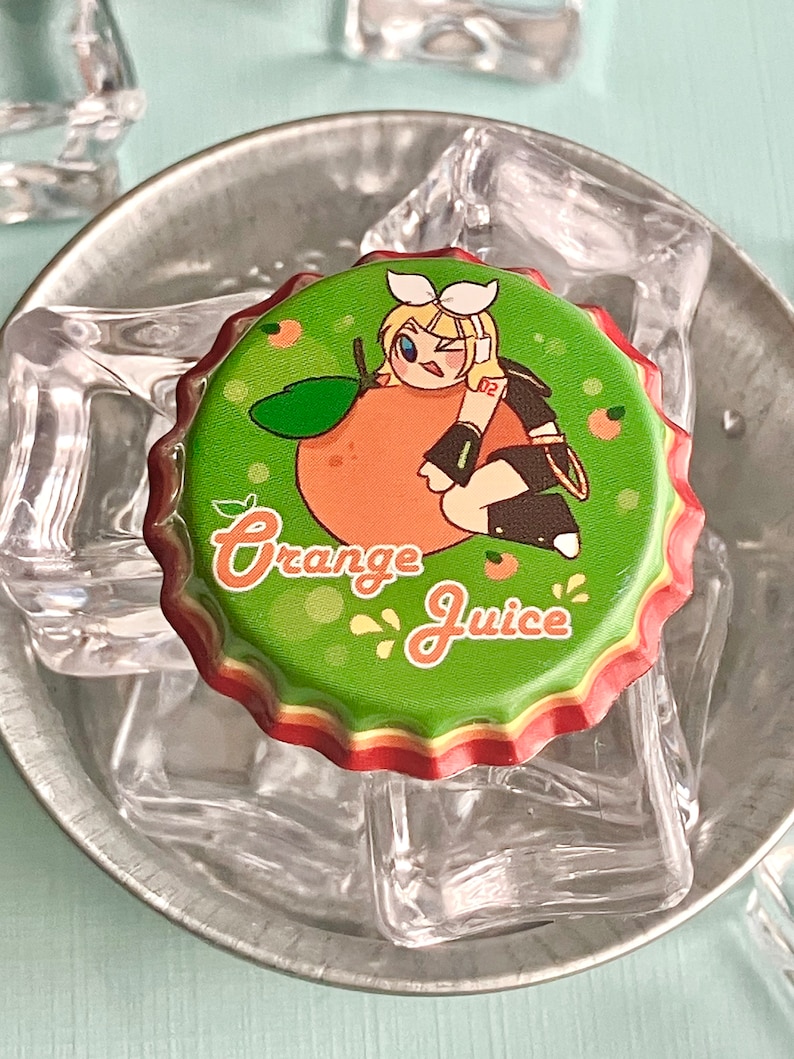 Puede incluir: Un tap&oacute;n de botella verde con una ilustraci&oacute;n de dibujos animados de una ni&ntilde;a sosteniendo una naranja. El texto "Orange Juice" est&aacute; impreso en el tap&oacute;n.