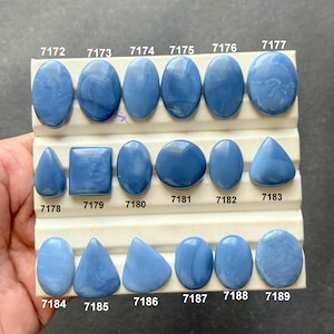 Könnte beinhalten: Eine Sammlung blauer Opal-Edelsteine in verschiedenen Formen, darunter oval, rund und dreieckig. Jeder Stein ist mit weißem Text nummeriert. Die Edelsteine werden auf einer weißen, mehrstufigen Oberfläche präsentiert.