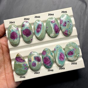 May include: A collection of ten oval and teardrop-shaped gemstones. Each stone features a vibrant magenta center surrounded by a mix of green and blue-green hues. The gemstones are labeled with numbers.