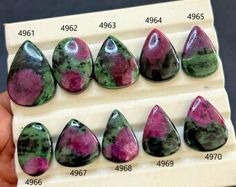 Può includere: Dieci pietre preziose di rubino zoisite lucide, ognuna con un motivo unico di rosso intenso, verde e nero. Le pietre sono a forma di goccia e ovali, esposte su una scheda bianca con etichette numerate.