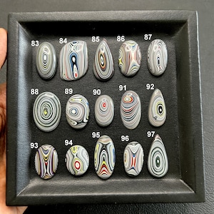 May include: A tray of 15 polished, colourful, and patterned agate cabochons. The cabochons are arranged in three rows of five. The cabochons are numbered 83 through 97.