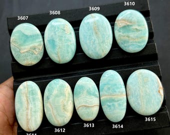 May include: A collection of ten oval-shaped Amazonite gemstones, each with unique patterns of blue-green hues and tan veining. The stones are displayed on a black tray, with each stone labeled with a number.