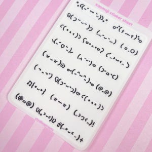 May include: A white sticker sheet with various black kaomoji emoticons. The sheet has the text "kaomoji sticker sheet" and "studiosprouts". The background is a pink and white striped pattern.