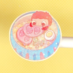 May include: A pink and white cartoon character with red hair is in a bowl of ramen. The ramen has pink and white meat, green vegetables, and a white egg. The bowl is decorated with blue and white stars.