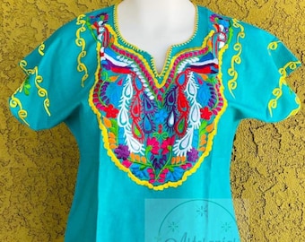 May include: A turquoise blue embroidered blouse with colorful floral and paisley designs. The embroidery is done in yellow, red, pink, blue, green, and white thread. The blouse has a V-neck and short sleeves.