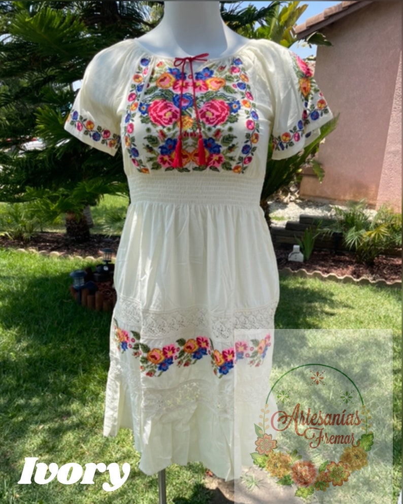 May include: A white embroidered dress with a floral design. The dress has short sleeves and a fitted bodice. The skirt is flowy and has a lace trim. The dress is made of cotton and is perfect for summer.
