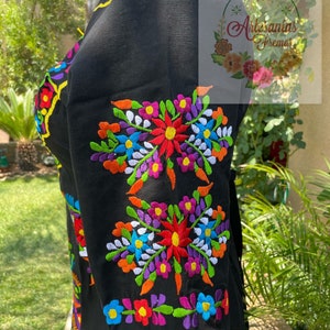 May include: Black embroidered blouse with colorful floral designs. The embroidery features a variety of colors, including red, orange, yellow, green, blue, purple, and white.