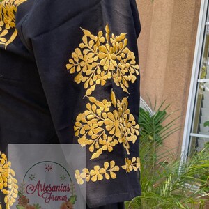 May include: Black cotton blouse with gold embroidered floral designs on the sleeves. The embroidery features a repeating pattern of flowers and leaves.