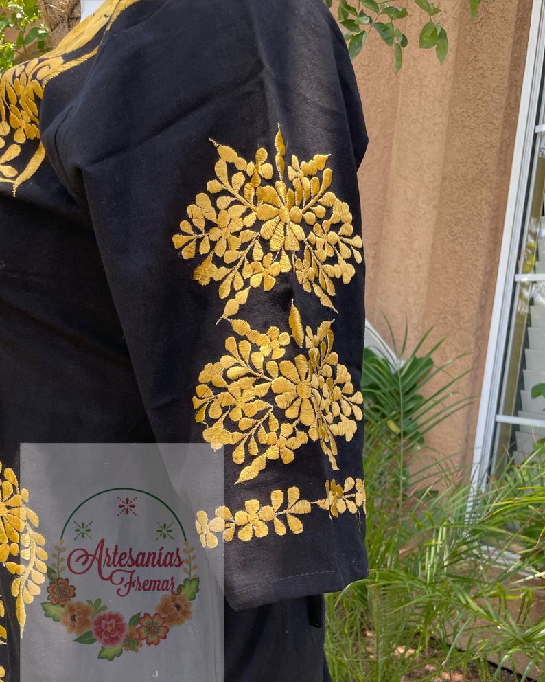 May include: Black cotton blouse with gold embroidered floral designs on the sleeves. The embroidery features a repeating pattern of flowers and leaves.