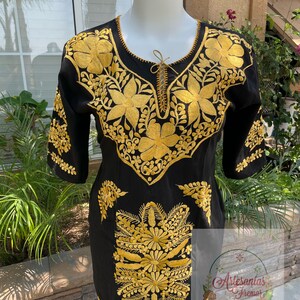 May include: Black cotton dress with gold embroidery of floral designs. The dress has a round neckline and three-quarter sleeves.