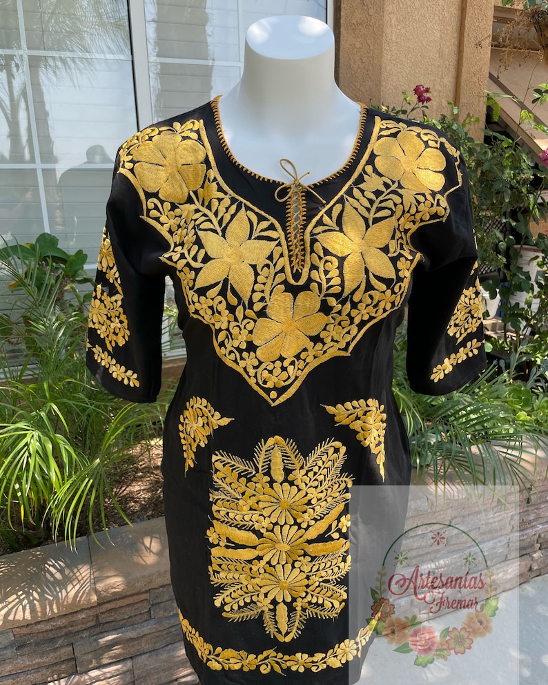 May include: Black cotton dress with gold embroidery of floral designs. The dress has a round neckline and three-quarter sleeves.