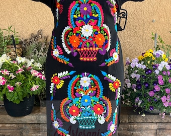 May include: Black embroidered dress with colorful floral and basket designs. The dress has short sleeves and a scoop neck. The embroidery is intricate and detailed, featuring a variety of colors, including red, orange, yellow, green, blue, purple, and white.