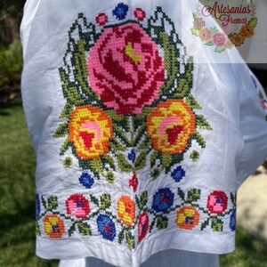 May include: White cotton blouse with colorful embroidered flowers. The embroidery features pink, red, yellow, orange, green, and blue thread.
