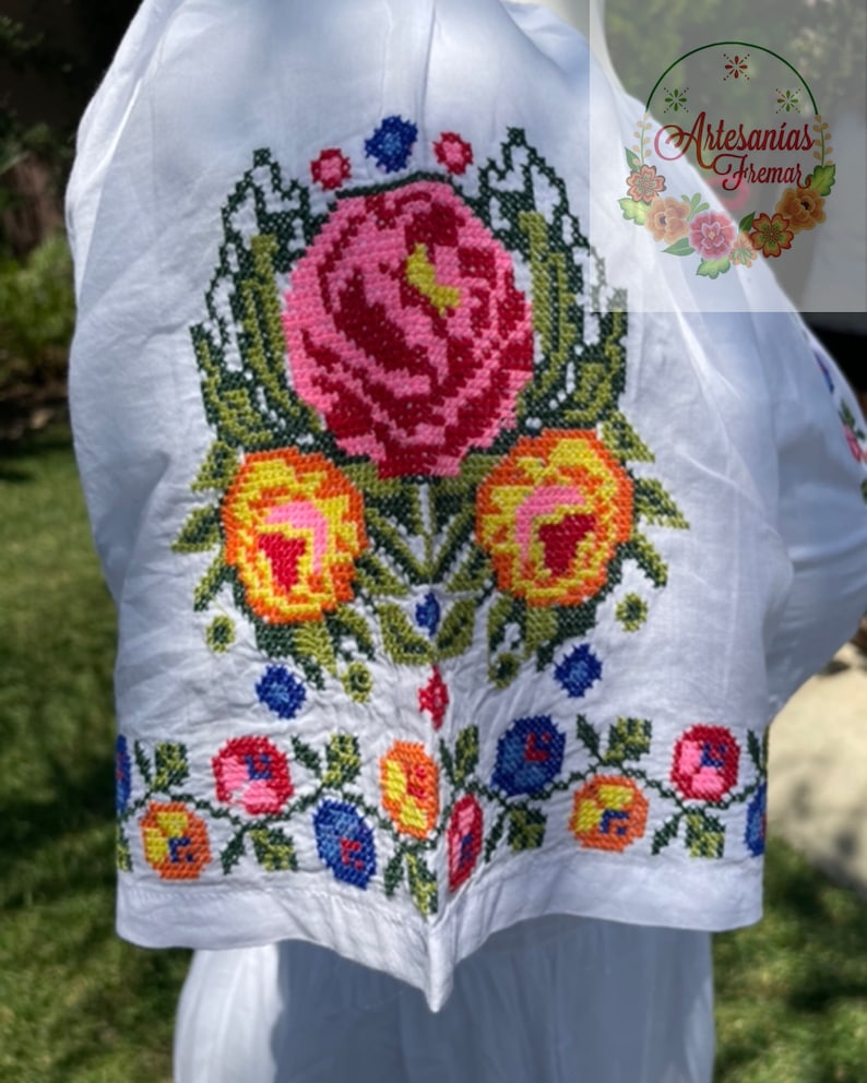 May include: White cotton blouse with colorful embroidered flowers. The embroidery features pink, red, yellow, orange, green, and blue thread.