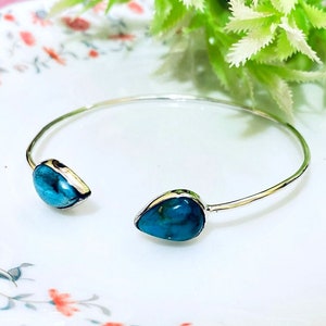 May include: A silver bangle bracelet with two turquoise teardrop-shaped stones.