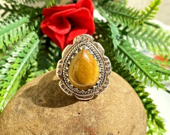 May include: A silver ring with a teardrop-shaped tiger's eye gemstone set in a detailed ornate design.