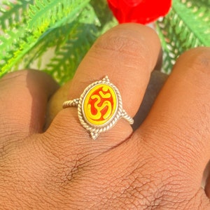 Puede incluir: Un anillo de plata con una incrustación ovalada de esmalte rojo y amarillo con el símbolo Om.