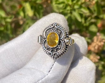 Könnte beinhalten: Ein silberner Ring mit einem gelben Edelstein, der in einem filigranen Design gefasst ist. Der Ring liegt auf einer weißen Oberfläche.