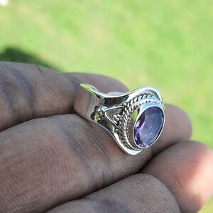 May include: A silver ring featuring an oval amethyst gemstone. The ring has an intricate design with a braided band and an ornate setting.
