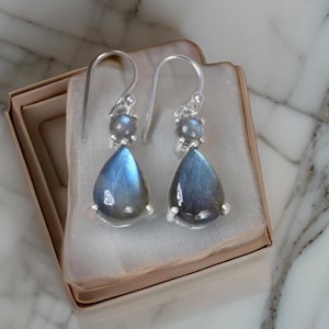 Puede incluir: Un par de pendientes de plata con piedras preciosas de labradorita en forma de lágrima. Los pendientes tienen una piedra preciosa de labradorita redonda más pequeña sobre la lágrima.