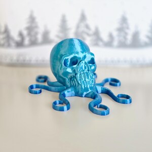 May include: A blue 3D printed skull with tentacles, resembling an octopus. The skull has a shiny, metallic finish.