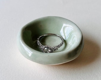 May include: A small, light green ceramic ring dish with a silver ring inside.