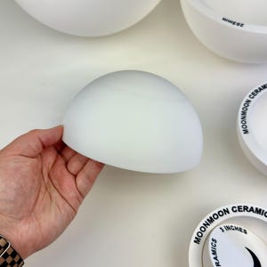 May include: A collection of white ceramic bowl molds in various sizes, including 3, 4, 7, 9, and 10 inches. Each mold features the text MOONMOON CERAMICS printed on the rim. The molds are hemispherical, smooth, and matte in texture.
