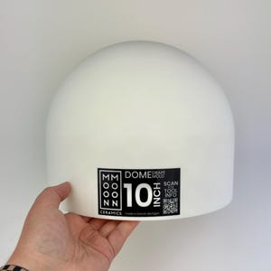 Może przedstawiać: Biała, gładka, kopułowa forma ceramiczna do drapowania. Czarna prostokątna etykieta z przodu zawiera tekst 'MOON CERAMICS', 'DOME DRAPE MOLD', '10 INCH' oraz 'SCAN FOR TOOL INFO' wraz z kodem QR. Forma posiada matowe wykończenie.