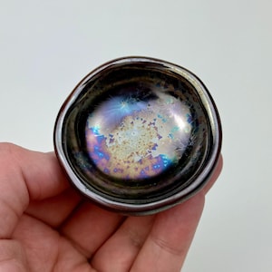 May include: A small, iridescent ceramic dish with a dark brown rim and a swirling pattern of blue, purple, and gold.